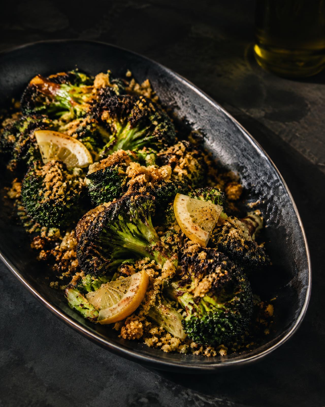 Charred broccoli with golden breadcrumbs and lemon on a dark platter