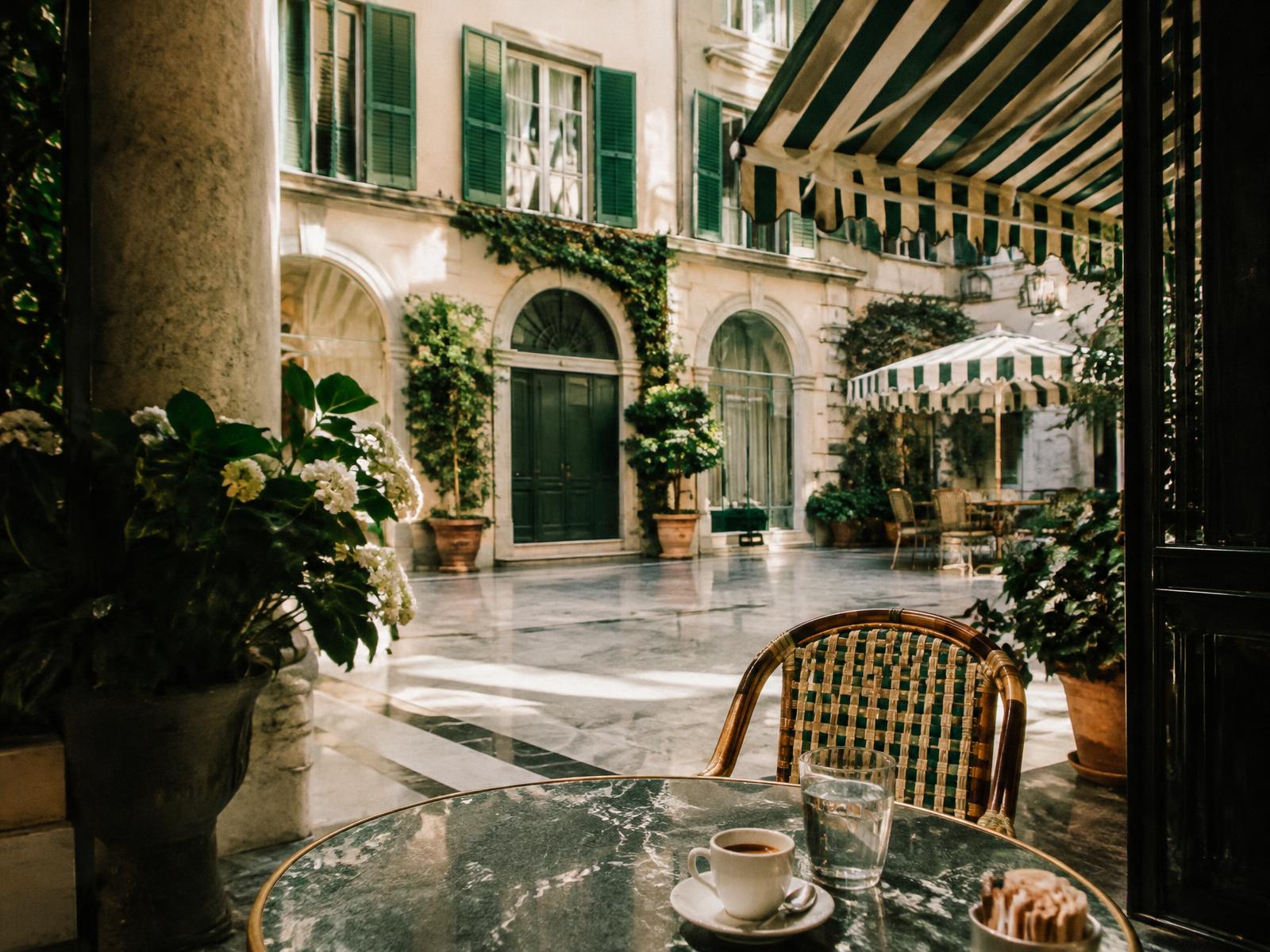 Milanese courtyard with green shutters, marble floor and a cafe table with espresso